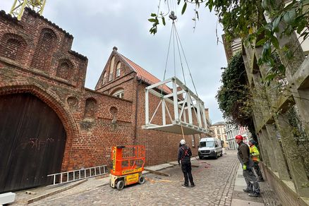 Eine Stahlkonstruktion wird in die Luft gehoben, im Hintergrund ein Backsteingebäude