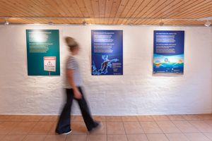 Eine Besucherin geht an drei blauen Wandtafeln vorbei