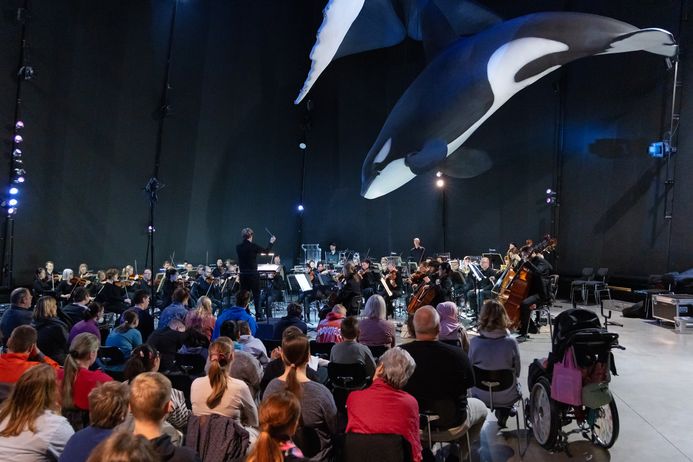 Orchester spiel vor Publikum unter einem hängenden Orca-Modell