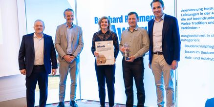 Gruppenbild: Fünf Personen stehen nebeneinander, zwei von ihnen halten Auszeichnungen in den Händen