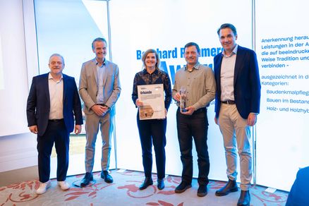 Gruppenbild: Fünf Personen stehen nebeneinander, zwei von ihnen halten Auszeichnungen in den Händen