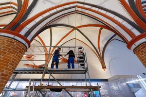 Personen stehen auf einer Rüstung unter einer Gewölbedecke