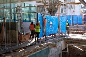 Mehrere Personen arbeiten auf einer Baustelle an einer in blaue Folie eingepackte Scheibe für ein Aquarium.