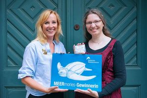 Zwei lächelnde Personen halten Plakat mit Schildkröten-Motiv in den Händen