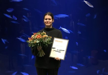 Vivian Fischbach steht mit Urkunde und Blumenstrauß vor einem Aquarium mit Fischen
