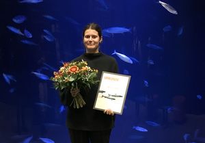 Vivian Fischbach steht mit Urkunde und Blumenstrauß vor einem Aquarium mit Fischen