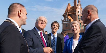 5 Personen in Anzügen schauen nach oben, im Hintergrund Backsteinhaus