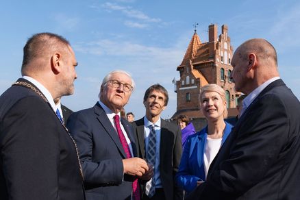 5 Personen in Anzügen schauen nach oben, im Hintergrund Backsteinhaus