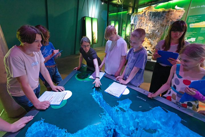 Frau zeigt einer Gruppe Jugendlicher den Relieftisch in der Ostsee-Ausstellung
