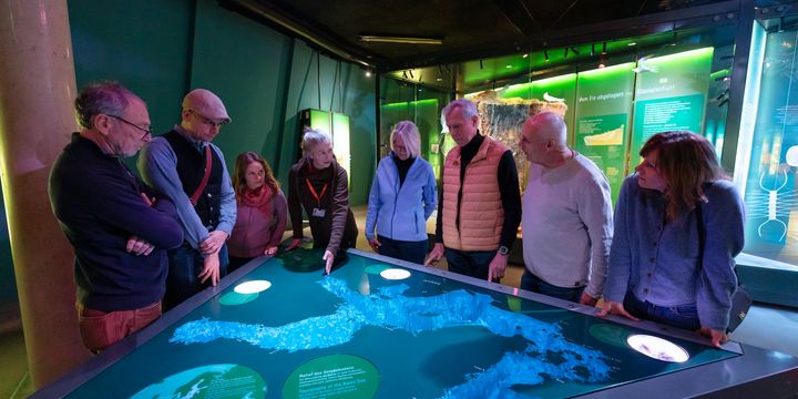 Eine Besuchergruppe steht im Museum vor einem illuminierten Thementisch, auf dem die Ostsee abgebildet ist. 