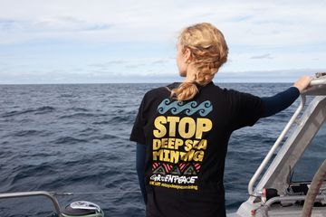 Eine Frau steht auf einem Boot uns blickt auf das Meer. Auf dem T-Shirt steht der Aufdruck: Stop Deep Sea Mining