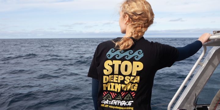 Eine Frau steht auf einem Boot uns blickt auf das Meer. Auf dem T-Shirt steht der Aufdruck: Stop Deep Sea Mining