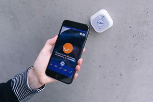 Eine Hand hält ein Smartphone neben einem Beacon an der Wand