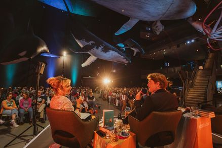 Zwei Personen sitzen auf einem Podium vor Publikum