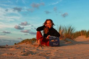 Eine Frau sitzt am Strand, mit dem Arm auf einem Buch lehnend