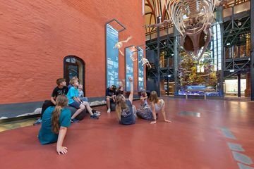 Eine Gruppe Jugendlicher in einer orangefarbenen Kirchenhalle unter einem hängenden Walskelett