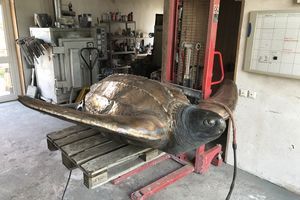 In einer Werkstatt steht auf einem Hebegerät eine bonzene Skulptur einer Schildkröte.