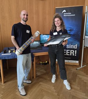 Eine Frau und ein Mann stehen vor einem Roll-Up des Deutschen Meeresmuseums und präsentieren Exponate zum Schweinswal.