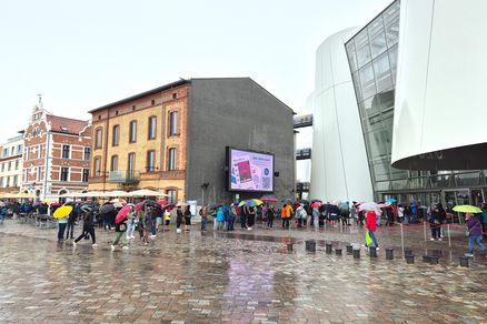 Gästeschlange im Regen vor einem weißen Gebäude