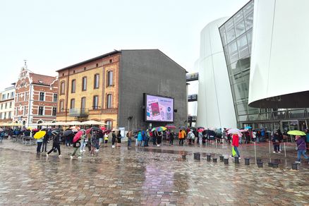 Gästeschlange im Regen vor einem weißen Gebäude