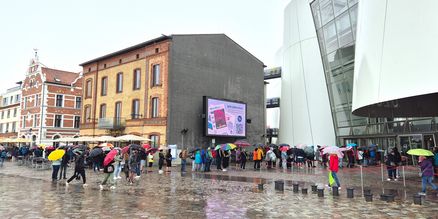 Gästeschlange im Regen vor einem weißen Gebäude
