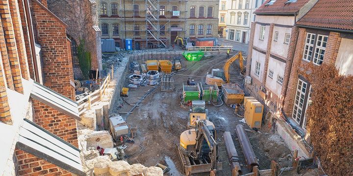 Blick auf eine Baustellengrube zwischen historischen Backsteinbauten. 