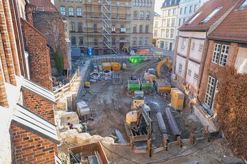 Blick auf eine Baustellengrube zwischen historischen Backsteinbauten. 