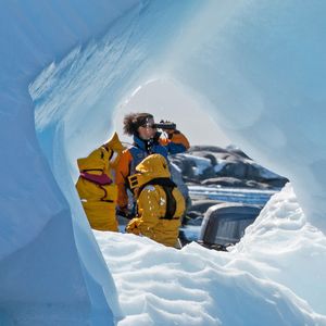 Blick durch ein Loch im Eis auf mehrere Menschen, darunter eine Frau, die durch ein Fernglas schaut. Foto: Dr. Maria Clauss 
