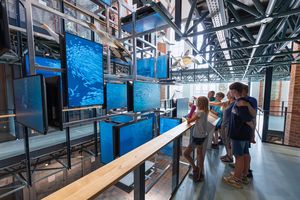 Personen stehen vor einer Brüstung und schauen auf Bildschirme mit blauen Unterwasserszenen