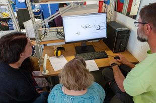 Drei Personen sitzen an einem Schreibtisch und schauen auf einen Computerbildschirm