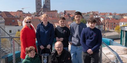Eine Gruppe auf einer Dachterrasse, im Hintergrund Dächer und Kirchengebäude einer Stadt
