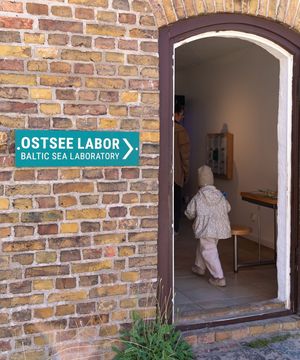 Eingang zum Ostsee-Labor im NATUREUM mit einem türkisfarbenen Hinweisschild an einer Backsteinwand.