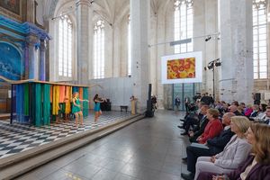 Menschen in einer Kirche vor einer bunten Kunstinstallation bestehend aus bunten Schnürsenkeln