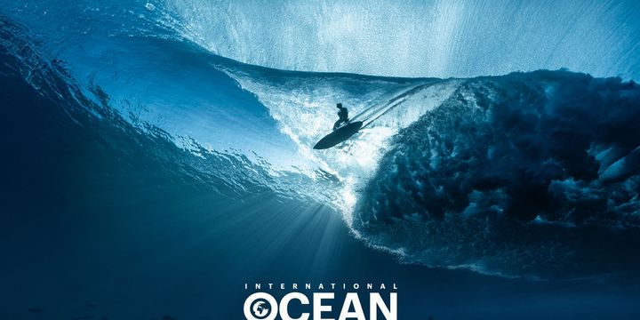 Surfer gleitet über einen blauen Ozean durch sphärisches Licht. 