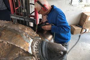 Der Bronzegiesser arbeitet mit dem Trennschleifer an einer bronzenen Skulptur einer Schildkröte.