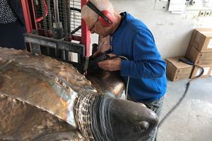 Der Bronzegiesser arbeitet mit dem Trennschleifer an einer bronzenen Skulptur einer Schildkröte.