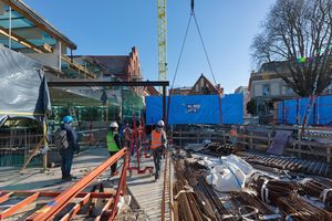 Blick auf eine Baustelle über die mit einem Turmdrehkran eine in blaue Folie eingepackte Scheibe für ein Aquarium gehoben wird.