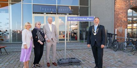 Vier Personen stehen an einem Straßenschild mit dem Titel "Harald-Lastovka-Platz"