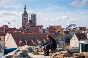 Eine Frau füttert Pinguine, im Hintergrund ein Stadtbild mit Kirche